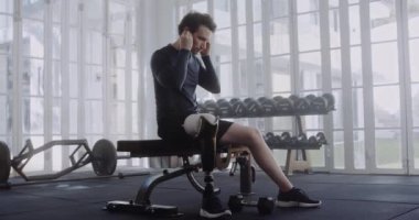 Egzersizden önce protez bacaklı beyaz bir erkek kulağına kulaklık takıyor. Modern tarzda spor yapan engelli bir sporcu..