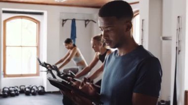 Genç siyah erkek, kapalı spor salonunda elektronik tablet kullanıyor. Kendine güvenen fitness profesyoneli.