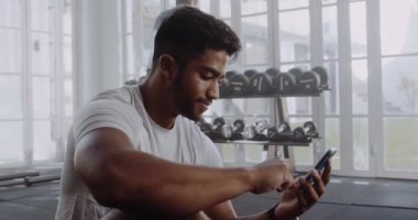 Modern tarz spor salonunda cep telefonuyla mesaj atan, gülümseyen ve gülen melez bir erkek..