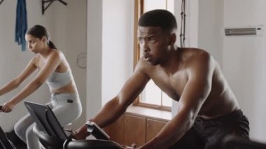 Siyah erkek, spor salonunda spor yaparken bisikletle çok çalışıyor. Arka planda meşgul spor salonu.