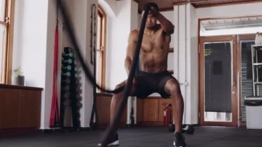 Güçlü, genç, siyah erkek, kapalı spor salonunda güç kazanmak için halat kullanıyor.