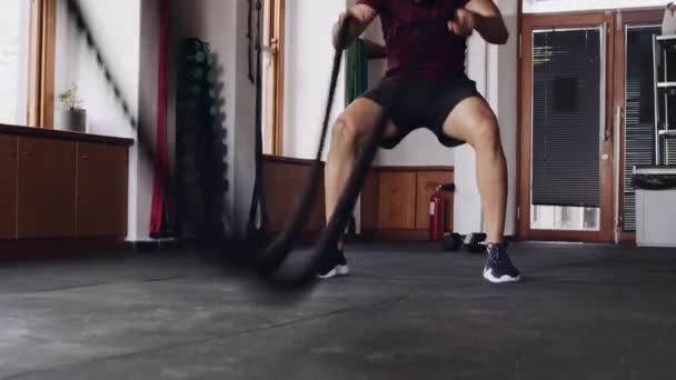 Silný a soustředěný mladý dospělý muž středního východu pomocí bojových lan získat sílu v kryté fitness tělocvičny — Stock video