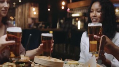 Çok ırklı bir arkadaş grubu bir restoranda bira bardaklarını tokuşturuyor..