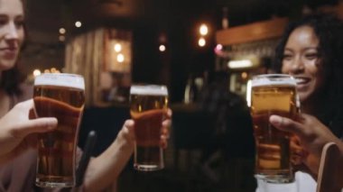 Çok ırklı bir arkadaş grubu bir restoranda bira bardaklarını tokuşturuyor..