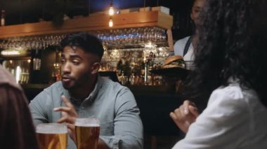Garson, restorandaki çok ırklı arkadaş grubuna yemeklerini getiriyor. Sonra bira bardaklarını tokuştururlar..