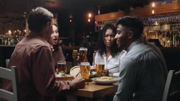 Μια πολυεθνική ομάδα φίλων που δειπνούν και πίνουν μπύρες σε ένα εστιατόριο και συζητούν ευχάριστα — Αρχείο Βίντεο