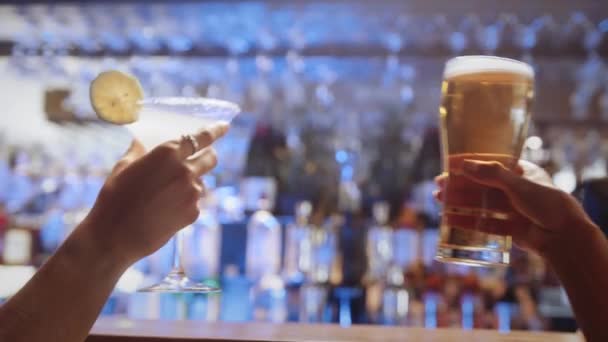 Primer plano de dos amigas tintineando sus copas de cóctel y cerveza en un bar. — Vídeo de stock