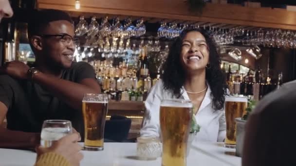 Un grupo multiétnico de amigos riendo y tomando cervezas en un restaurante. — Vídeos de Stock