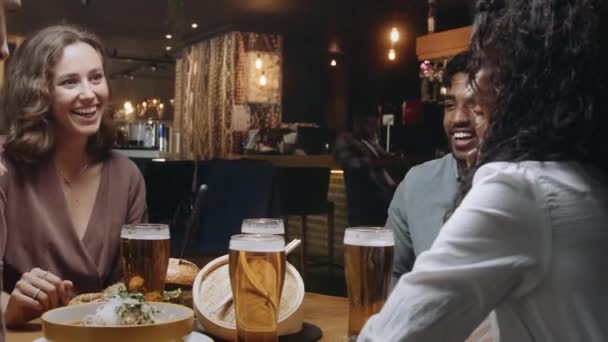 Multi-ethnische Gruppe von Freunden beim Essen und Trinken in einem Restaurant. Kellnerin im Hintergrund bringt den Rest ihres Essens. — Stockvideo
