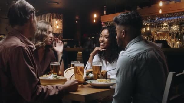 Een multi-etnische groep vrienden die een biertje drinken en dineren in een restaurant en een aangenaam gesprek voeren — Stockvideo