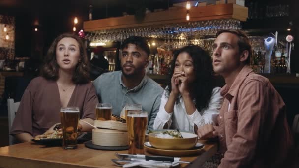 Un groupe multi-ethnique d'amis regardant un match de sport à la télévision dans un restaurant. Ils s'applaudissent et se surpassent quand leur équipe marque.. — Video