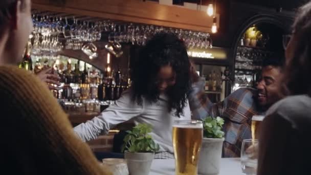 Multiracial žena se připojí ke skupině přátel v restauraci na nápoje. Pozdravuje a objímá své přátele, když přijde. — Stock video