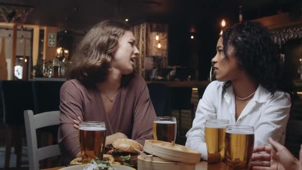 Zwei schöne birassische Frauen unterhalten sich in einem Restaurant beim Abendessen mit Freunden. — Stockvideo