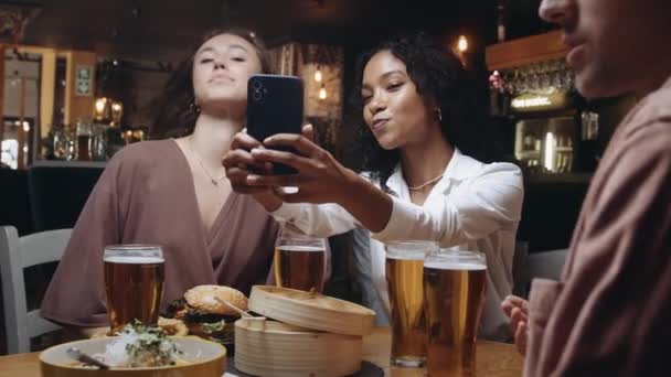 Zwei multiethnische Freunde machen ein Selfie in einem Restaurant. Sie sehen sich die Fotos an, die sie danach gemacht haben. — Stockvideo