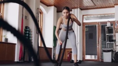 Determined young adult biracial female using battle ropes to gain strength at an indoor fitness gym