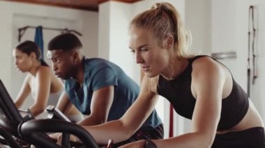 Caucasian female cycling on stationary bike in a group fitness class at an indoor fitness gym. Having a good time and determined.