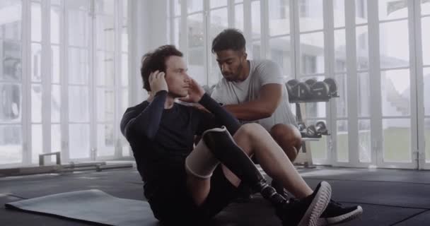 Caucasian male with prosthetic leg doing sit ups with trainer in modern style gym — Vídeo de stock