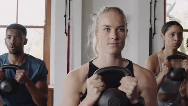 Fit e grupo saudável de jovens adultos diversos agachados com kettlebell em um ginásio de fitness indoor. — Vídeo de Stock