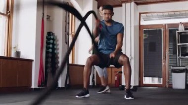 Kapalı spor salonunda savaş halatları kullanan kararlı siyah bir erkek. Kardiyovasküler zindelik, sıkı çalışma. 