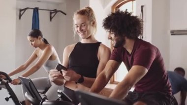 Beyaz, genç, yetişkin bir kadın cep telefonuyla orta doğulu bir erkekle spor salonunda selfie çekiyor.. 