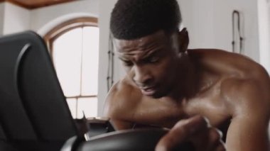 Genç zenci erkek spor salonunda egzersiz bisikleti üzerinde çok çalışıyor. Kararlı ve odaklı. 