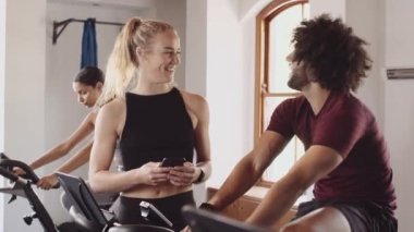 Beyaz kadın, spor salonunda bisiklet sürerken Orta Doğulu bir erkekle sohbet ediyor. Ona cep telefonu görüntülerini gösteriyorum.. 