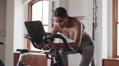 Genç, çift ırklı bir kadın spor salonunda stabil egzersiz bisikleti üzerinde bisiklet egzersizini bitiriyor.. 