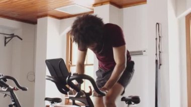 Orta Doğulu genç bir erkek spor salonunda spor salonunda kararlı ve yorgun bir şekilde bisiklet sürüyor.. 