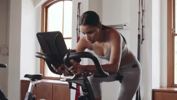 在室内健身馆的固定锻炼自行车上 年轻的成年女子骑完自行车运动 — 图库视频影像