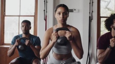Spor salonunda kettlebell ile grup fitness dersinde çömelmiş genç yetişkinlerden oluşan çok kültürlü bir grup. Odaklanmış ve sığdırılmış. 