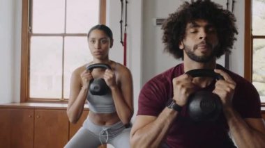 Odaklanmış Orta Doğulu adam ve çeşitli arkadaş grupları kapalı spor salonunda kettlebell ile çömeliyor.. 