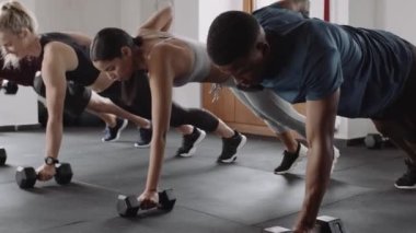 Bir grup farklı yetişkin arkadaş kapalı spor salonunda egzersiz yapıyorlardı. Kalas pozisyonunda ağırlık kaldırılıyor. 