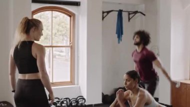 Diverse group of individuals in group exercise class being coached by trainer at indoor fitness gym. Squatting with friends. 