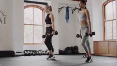 Group of diverse, fit friends exercising together at indoor fitness gym. Lunges with weights and celebrations afterwards. 