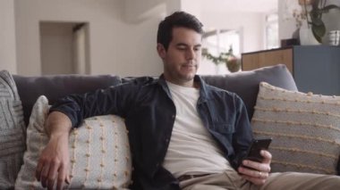 Kafkasyalı bir adam evdeki koltukta dinleniyor. Cep telefonuyla sosyal medyada gezinirken gülümsüyor. Yüksek kalite 4k görüntü