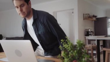 Yakışıklı beyaz adam evde yemek masasında oturur ve dizüstü bilgisayarı üzerinde çalışmaya başlar. Yüksek kalite 4k görüntü