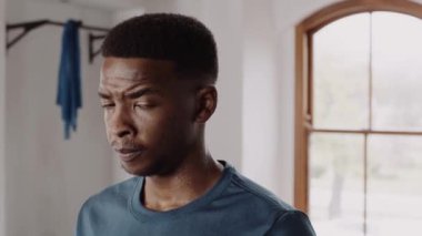 Fit and healthy black male exhaling and looking at camera seriously. Post-workout at indoor fitness gym. 