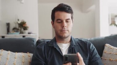 Caucasian man relaxing sitting on couch at home while using social media on his mobile phone. High quality 4k footage