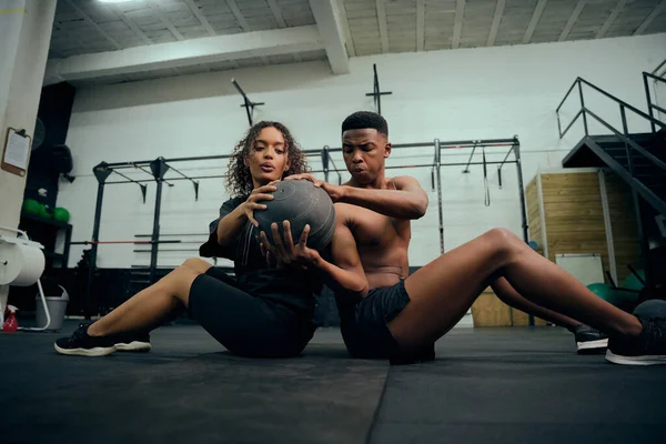 多种族的朋友在体育馆做交叉适合的运动 非裔美国男性和女性坐在地板上 在锻炼过程中通过药物球 高质量的照片 高质量的照片 — 图库照片
