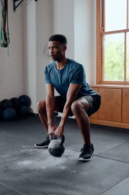 Determined muscular young black man in sportswear doing kettlebell squats at the gym