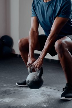 Close up of muscular young black man in sportswear doing kettlebell squats at the gym