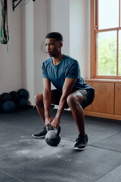 Determined muscular young black man in sportswear doing kettlebell squats at the gym