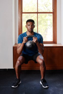 Determined young black man in sportswear doing kettlebell squats at the gym