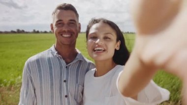 Happy young couple smiling and talking during travel vlog by agricultural field