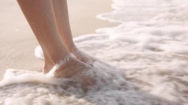 Close-up of young biracial woman standing barefoot in sea by beach