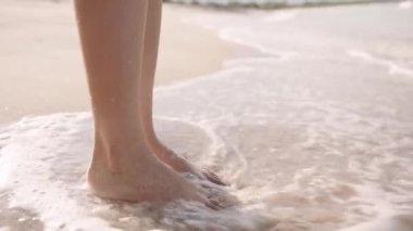 Close-up of young biracial woman standing barefoot in water on beach
