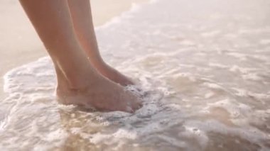 Close-up of barefoot young biracial woman standing in sea by beach