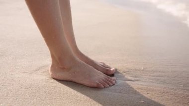 Close-up of young biracial woman barefoot on beach by sea
