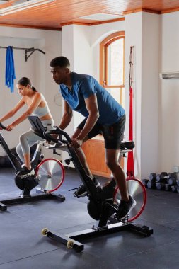 Spor giyimli atletik siyah erkek ve çift ırklı kadın spor salonunda egzersiz bisikleti kullanıyorlar.