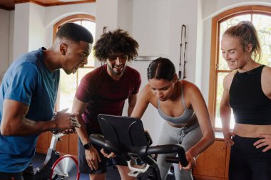 Spor kıyafetleri içinde kendinden emin genç yetişkinler spor salonunda spor bisikletli bir arkadaşı motive ediyor.